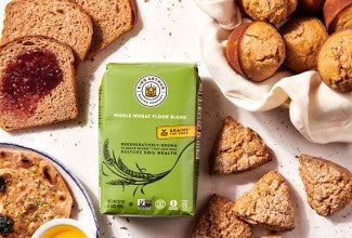 A bag of Climate Blend Flour surrounded by bakes goods made with it, including muffins, scones, flatbread, and sandwich bread